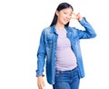 Young beautiful chinese woman pregnant expecting baby doing peace symbol with fingers over face, smiling cheerful showing victory