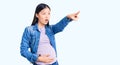 Young beautiful chinese woman pregnant expecting baby pointing with finger surprised ahead, open mouth amazed expression, Royalty Free Stock Photo