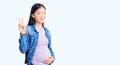 Young beautiful chinese woman pregnant expecting baby smiling looking to the camera showing fingers doing victory sign