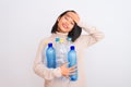 Young beautiful chinese woman recycling plastic bottles over isolated white background stressed with hand on head, shocked with