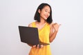 Young beautiful chinese woman using laptop standing over isolated white background pointing and showing with thumb up to the side Royalty Free Stock Photo