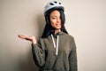 Young beautiful chinese woman wearing bike helmet over isolated white background smiling cheerful presenting and pointing with Royalty Free Stock Photo