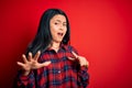 Young beautiful chinese woman wearing casual shirt over isolated red background afraid and terrified with fear expression stop Royalty Free Stock Photo