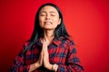 Young beautiful chinese woman wearing casual shirt over isolated red background begging and praying with hands together with hope Royalty Free Stock Photo