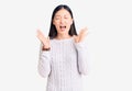 Young beautiful chinese woman wearing casual sweater celebrating mad and crazy for success with arms raised and closed eyes