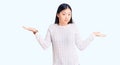 Young beautiful chinese woman wearing casual sweater clueless and confused expression with arms and hands raised