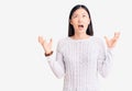 Young beautiful chinese woman wearing casual sweater crazy and mad shouting and yelling with aggressive expression and arms raised