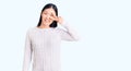 Young beautiful chinese woman wearing casual sweater doing peace symbol with fingers over face, smiling cheerful showing victory