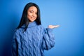 Young beautiful chinese woman wearing casual sweater over isolated blue background smiling cheerful presenting and pointing with Royalty Free Stock Photo