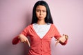 Young beautiful chinese woman wearing casual sweater over isolated pink background Pointing down looking sad and upset, indicating Royalty Free Stock Photo