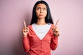 Young beautiful chinese woman wearing casual sweater over isolated pink background Pointing up looking sad and upset, indicating Royalty Free Stock Photo