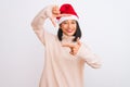 Young beautiful chinese woman wearing Christmas Santa hat over isolated white background smiling making frame with hands and Royalty Free Stock Photo