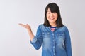 Young beautiful chinese woman wearing denim shirt over isolated white background smiling cheerful presenting and pointing with Royalty Free Stock Photo