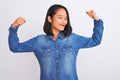 Young beautiful chinese woman wearing denim shirt standing over isolated white background showing arms muscles smiling proud Royalty Free Stock Photo