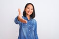 Young beautiful chinese woman wearing denim shirt standing over isolated white background smiling friendly offering handshake as Royalty Free Stock Photo