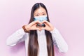 Young beautiful chinese woman wearing medical mask smiling in love doing heart symbol shape with hands Royalty Free Stock Photo