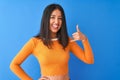 Young beautiful chinese woman wearing orange t-shirt standing over isolated blue background smiling doing phone gesture with hand Royalty Free Stock Photo