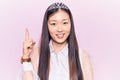 Young beautiful chinese woman wearing princess crown smiling with an idea or question pointing finger up with happy face, number