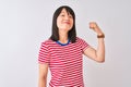 Young beautiful chinese woman wearing red striped t-shirt over isolated white background Strong person showing arm muscle, Royalty Free Stock Photo