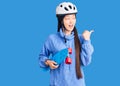 Young beautiful chinese woman wearing security helmet holding skate pointing thumb up to the side smiling happy with open mouth