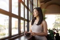 Young beautiful Asian woman having a coffee break while leaning against the windows Royalty Free Stock Photo