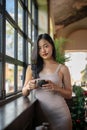 Young beautiful Asian woman having a coffee break while leaning against the windows Royalty Free Stock Photo