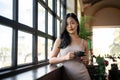 Young beautiful Asian woman having a coffee break while leaning against the windows Royalty Free Stock Photo