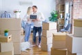 Young beautiful couple with dog standing holding blackboard with message kissing at new home around cardboard boxes