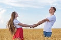 Young beautiful couple in field holding hands and lovingly looking at each other. Weekend in countryside Royalty Free Stock Photo