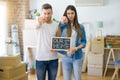 Young beautiful couple holding blackboard with our first home text at new house pointing with finger to the camera and to you, Royalty Free Stock Photo
