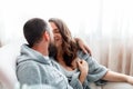 Young beautiful couple hug kissing while sitting on couch at cozy home interior. Married man and woman romantic Royalty Free Stock Photo