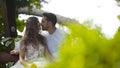 Young beautiful couple kissing on bench in garden. Action. Young husband and wife gently kissing on bench in green Royalty Free Stock Photo