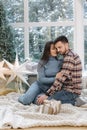 Young and beautiful couple of man and woman sitting in front of big windor, it's snow outside. Happy family at Christmas Royalty Free Stock Photo