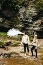 Young and beautiful couple at the mountain waterfall - Happy tourists visiting mountains. Lovestory. Tourists in hats. Military