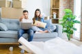 Young beautiful couple relaxing sitting on the sofa of new house using computer laptop pointing with finger to the camera and to Royalty Free Stock Photo