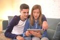 Young beautiful couple 20s using digital tablet pad computer sitting at home couch living room shopping on line choosing items on Royalty Free Stock Photo