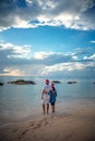 Young beautiful couple in Santa Claus hats walks along the shore of the tropical sea at sunset in the resort, vacation and travel Royalty Free Stock Photo