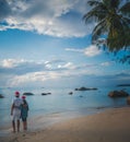 Young beautiful couple in Santa Claus hats walks along the shore of the tropical sea at sunset in the resort, vacation and travel Royalty Free Stock Photo