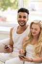 Young Beautiful Couple Sit On Coach Near Window, Using Cell Smart Phone Happy Smile Hispanic Man Woman Royalty Free Stock Photo