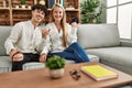 Young beautiful couple sitting on the sofa at home pointing thumb up to the side smiling happy with open mouth Royalty Free Stock Photo