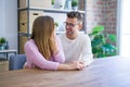 Young beautiful couple sitting on the table at home, hugging in love very happy for moving to new home with cardboard boxes behind Royalty Free Stock Photo