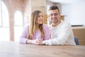 Young beautiful couple sitting on the table at home, hugging in love very happy for moving to new home with cardboard boxes behind Royalty Free Stock Photo