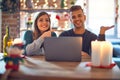 Young beautiful couple sitting using laptop around christmas decoration at home amazed and smiling to the camera while presenting Royalty Free Stock Photo