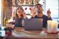 Young beautiful couple sitting using laptop around christmas decoration at home amazed and surprised looking up and pointing with Royalty Free Stock Photo