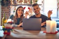 Young beautiful couple sitting using laptop around christmas decoration at home with a big smile on face, pointing with hand and Royalty Free Stock Photo