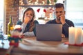 Young beautiful couple sitting using laptop around christmas decoration at home looking stressed and nervous with hands on mouth Royalty Free Stock Photo