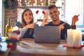 Young beautiful couple sitting using laptop around christmas decoration at home smiling and looking at the camera pointing with Royalty Free Stock Photo