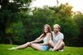 Young beautiful couple smiling, sitting on grass in park. Outdoor background. Royalty Free Stock Photo