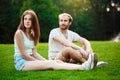 Young beautiful couple smiling, sitting on grass in park. Outdoor background. Royalty Free Stock Photo