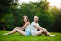 Young beautiful couple smiling, sitting on grass in park. Outdoor background. Royalty Free Stock Photo